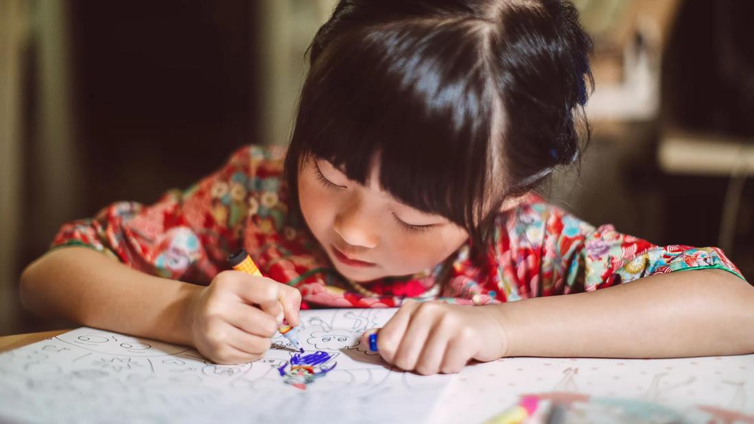 Child bent over coloring book, coloring with a marker