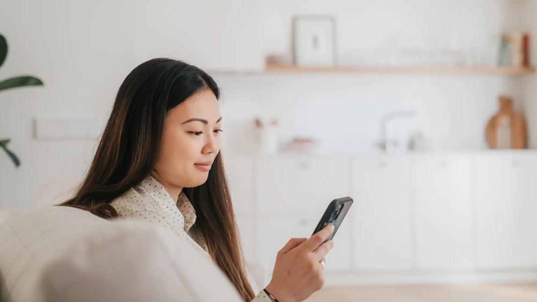 Smiling person looking at their phone, sitting on couch