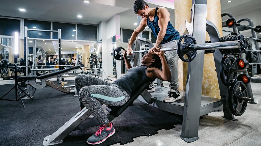 Person spotting a person doing an inclined bench press in gym