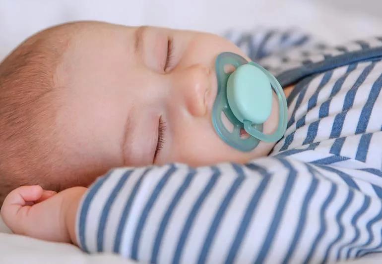Baby sleeping on back sucking on pacifier.