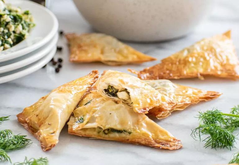 Spinach filled spanakopitas on a white marble table.