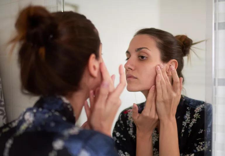 A person checking their skin for blemishes while looking at a mirror