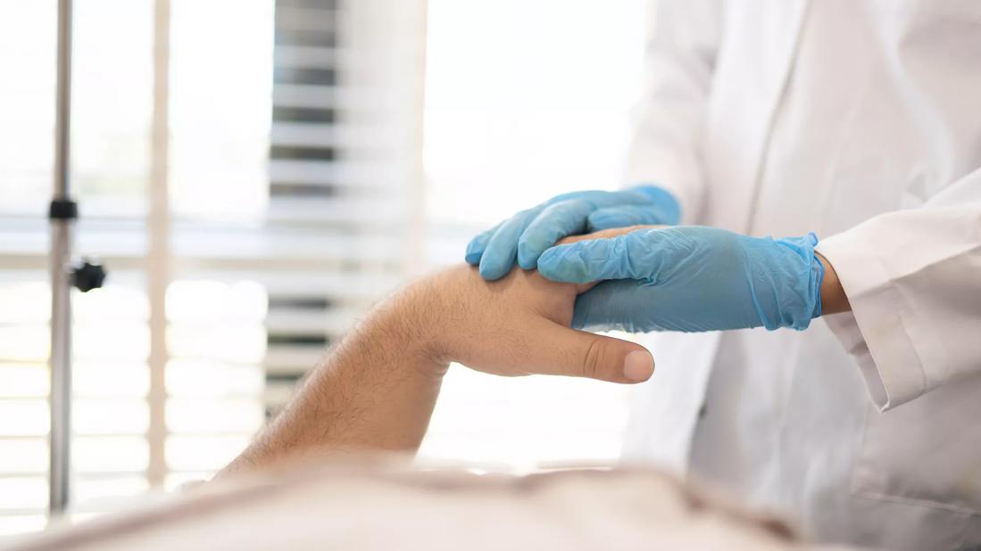 Healthcare provider in gloves holding hand of patient in hospital bed