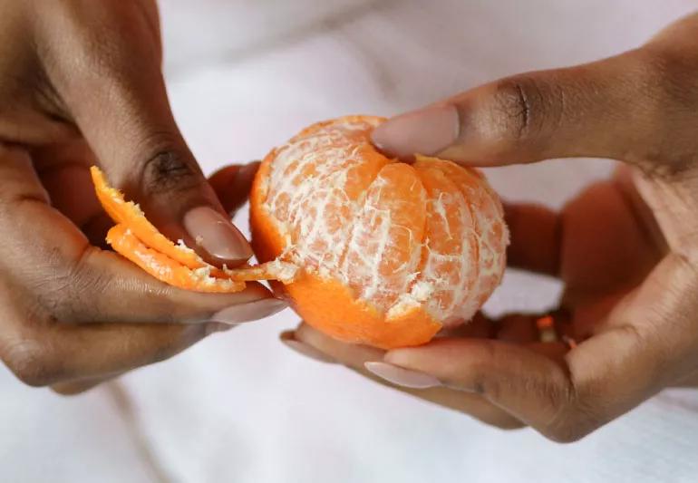 Person peeling an orange, which has a higher sugar content.