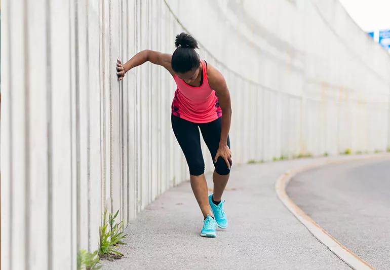 A runner leaning against a wall holding their knee