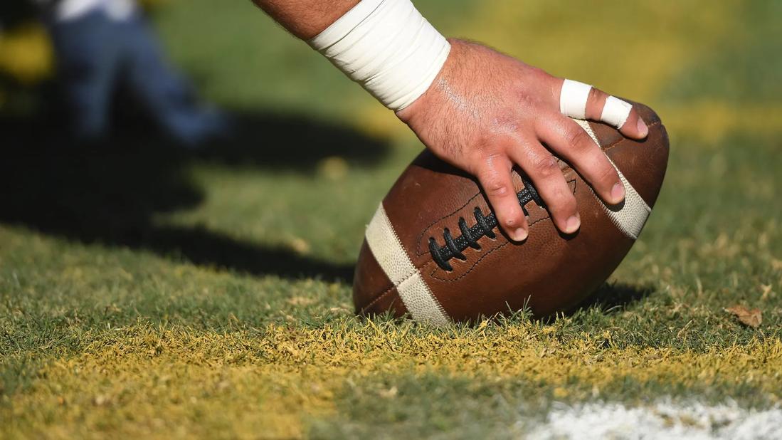 Large hand with athlete-taped wrist and fingers gripping football on the field