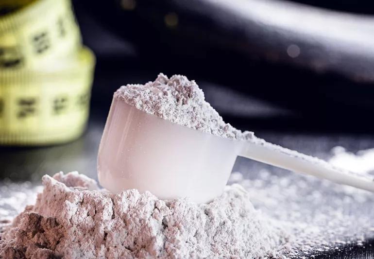 A scoop of creotine powder in the foreground of a gym table.