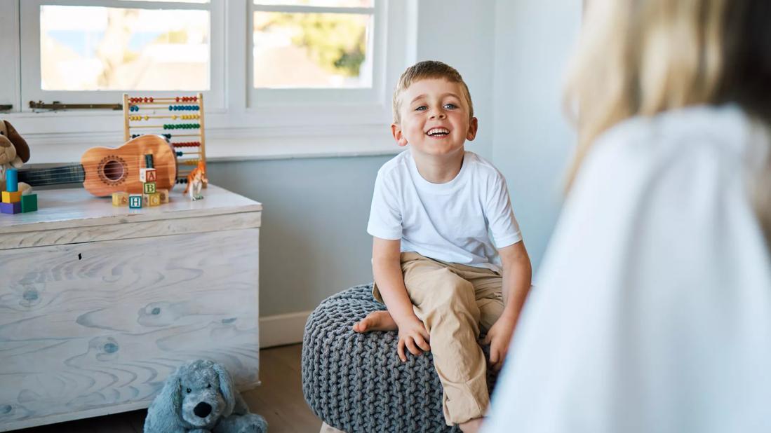 Happy child sitting on stool in healthcare office, with toys around