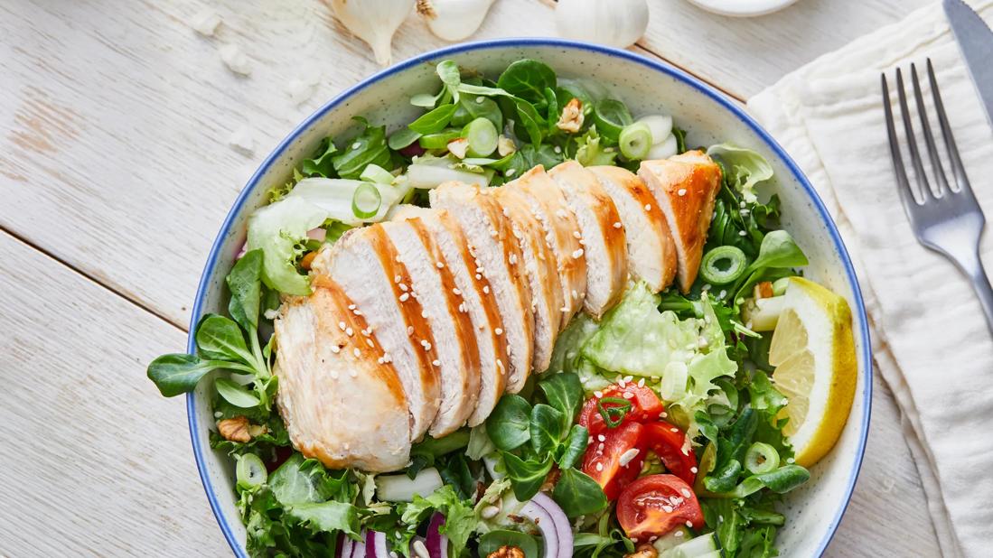 Sliced grilled chicken sprinkled with sesame seeds over mixed greens with tomatoes and onions