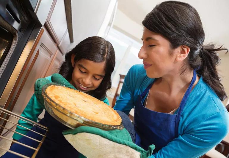 Mother a daughter remove pie from hot kitchen oven