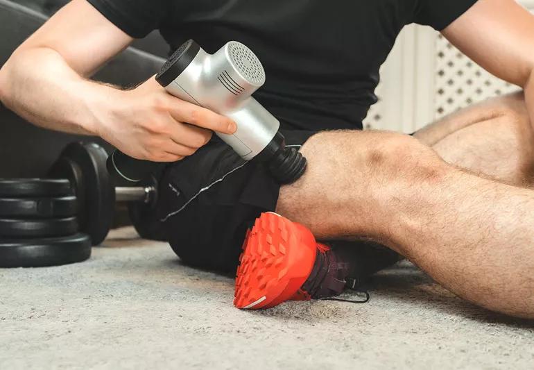 man using massage gun after lifting weights