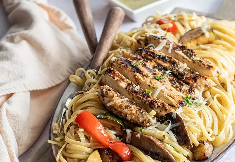 Linguine topped with chicken strips, shredded cheese and colorful vegetables