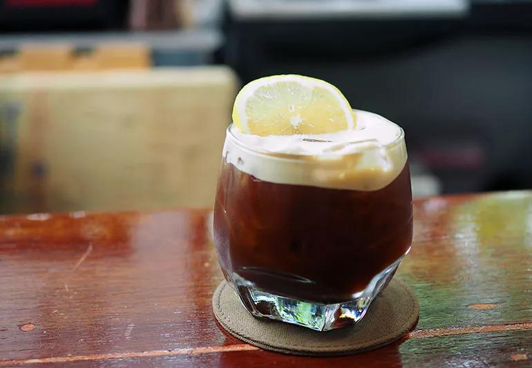 Coffee in a clear glass with foam and a lemon on top