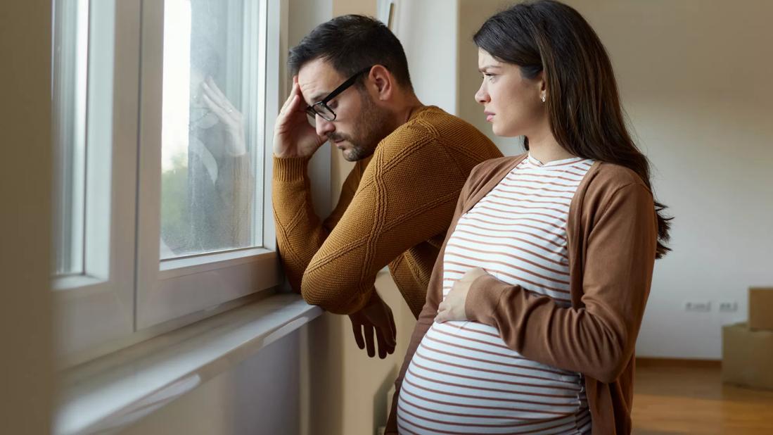 Male and pregnant female looking out window pensively