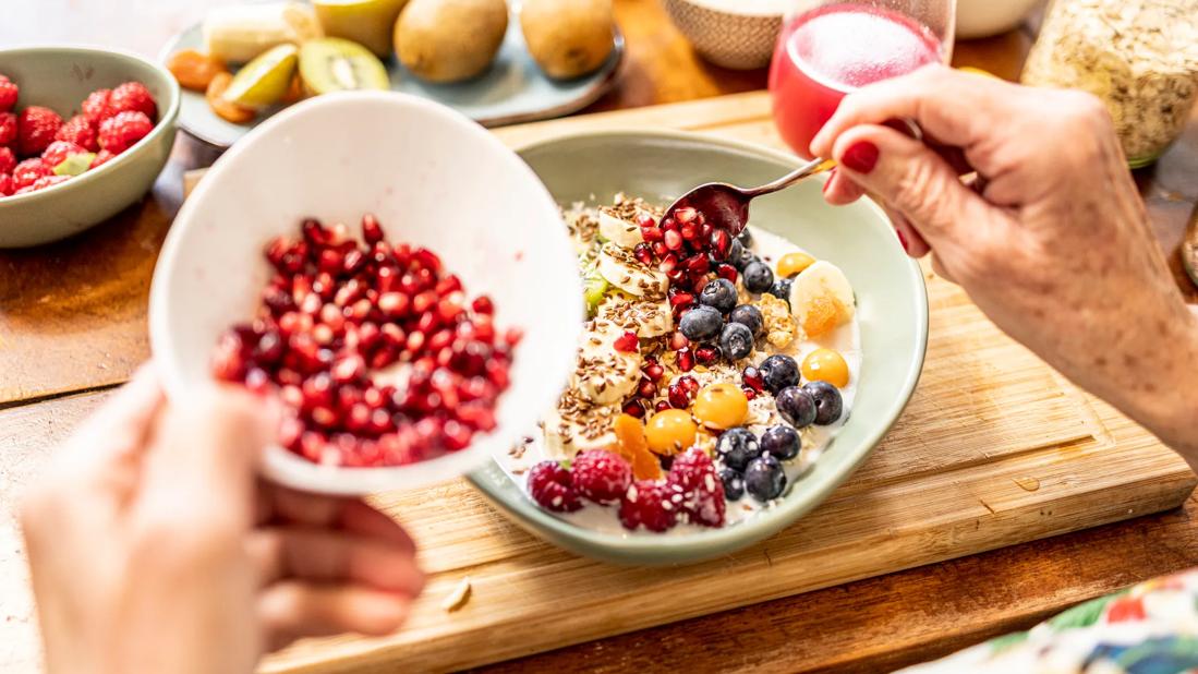 Hands scooping pomegranate seeds from bowl onto fruit bowl