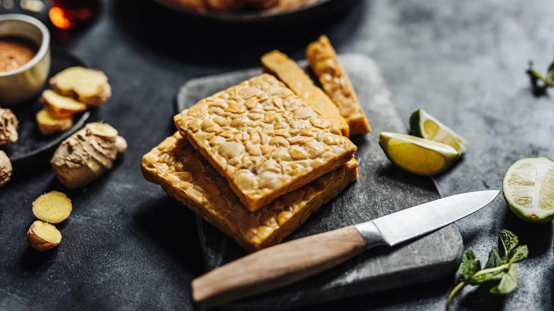 Two cakes of tempeh on black cutting board, with lime and knife