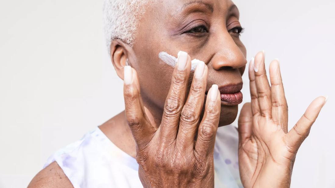 Older person applying skin cream to their face