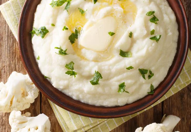 Overhead closeup of cauliflower pseudo mashed potatoes in a bowl on a wooden table.