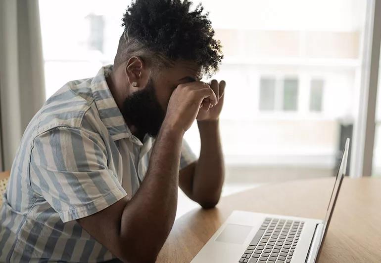 A person sitting by a computer rubbing their eyes