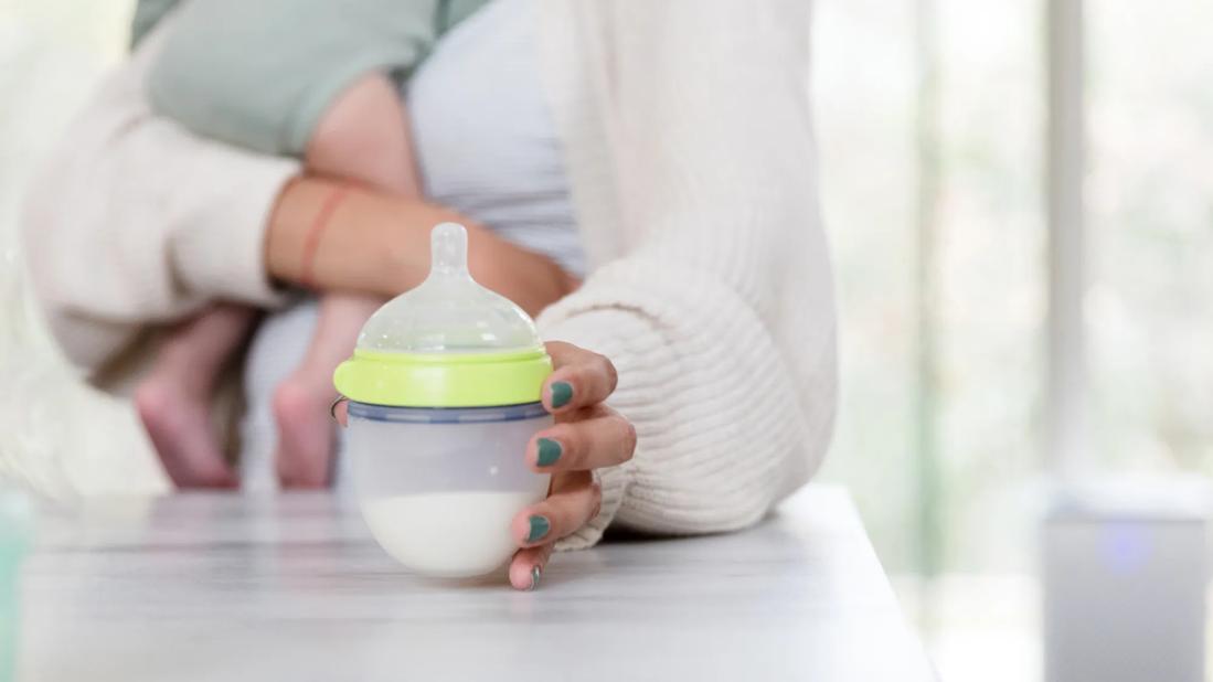 Caregiver holding baby and picking up bottle of milk