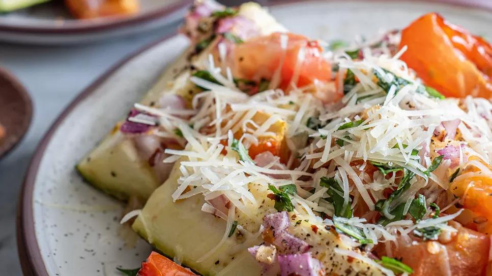 Closeup of roasted garlic tomato zucchini bake on a stoneware plate with grated cheese garnish