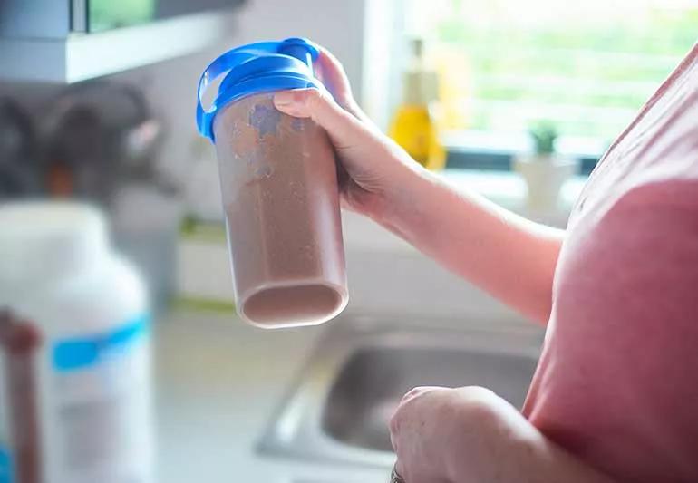 Person preparing a protein shake in kitchen.