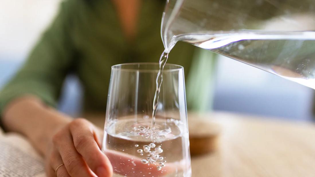 Person pouring a glass of water from a glass pitcher