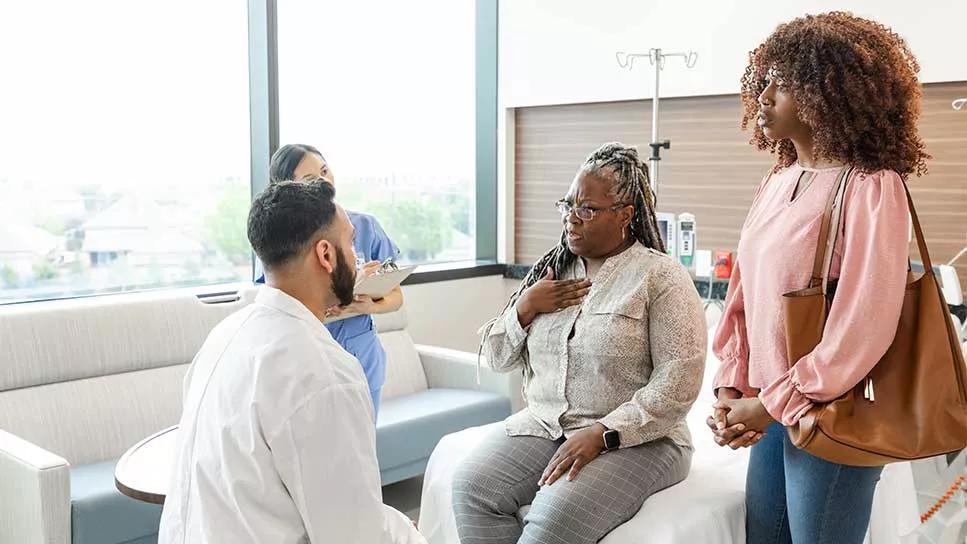 seated doctor and female in doctor office, with female's hand on heart, with daughter