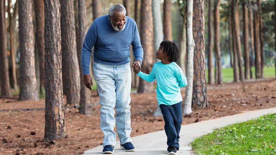 Elderly person walks with grandson on path in woods