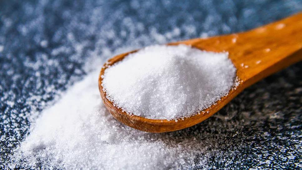 A wooden spoonful of salt on a granite tabletop with salt scattered around