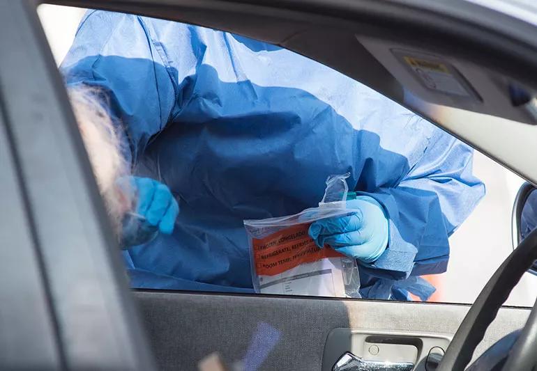 A person sitting in their car while a healthcare worker swabs their nose for a COVID-19 test