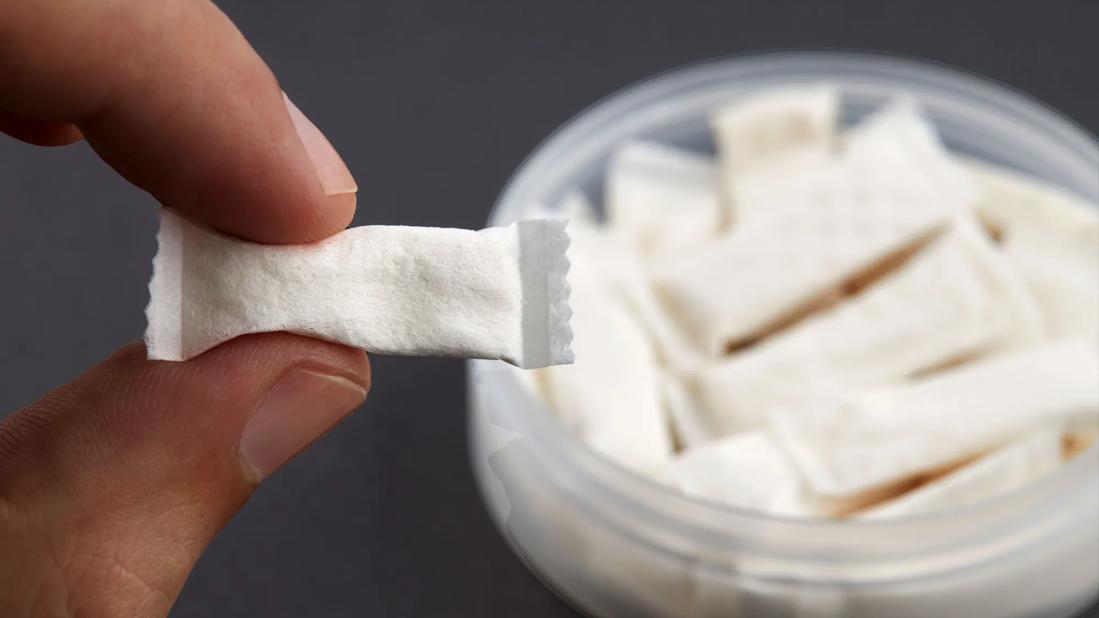 Fingers holding a nicotine pouch in front of container of nicotine pouches