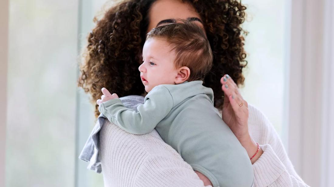 Caregiver burping baby, holding baby over their shoulder, patting baby's back