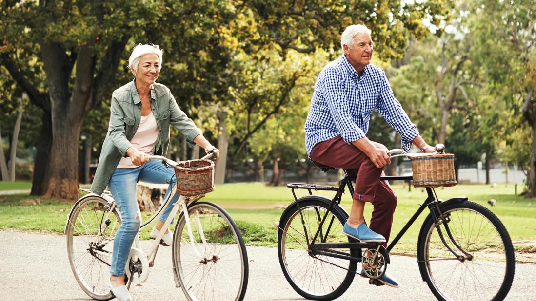 Older man and woman riding bikes with baskets in park