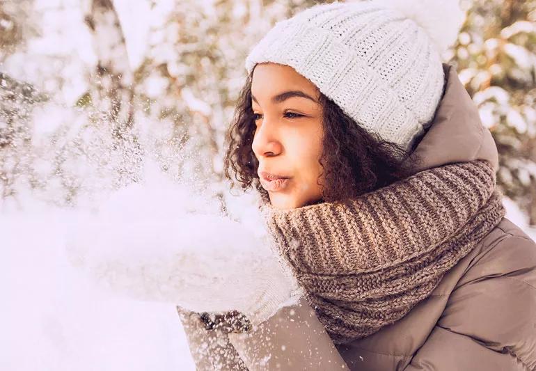 Person blowing snow off of gloved hands while outside during cold winter weather.