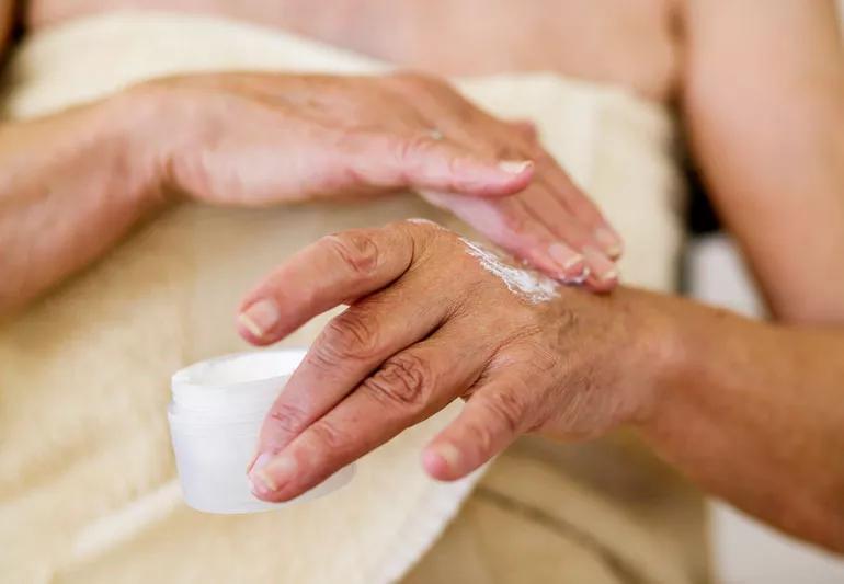 close up of hands of person applying moisturizer