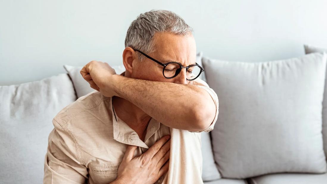 Person coughing into their elbow, with hand on their chest