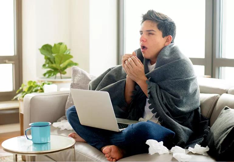 Man coughing and sneezing while sitting on couch at home