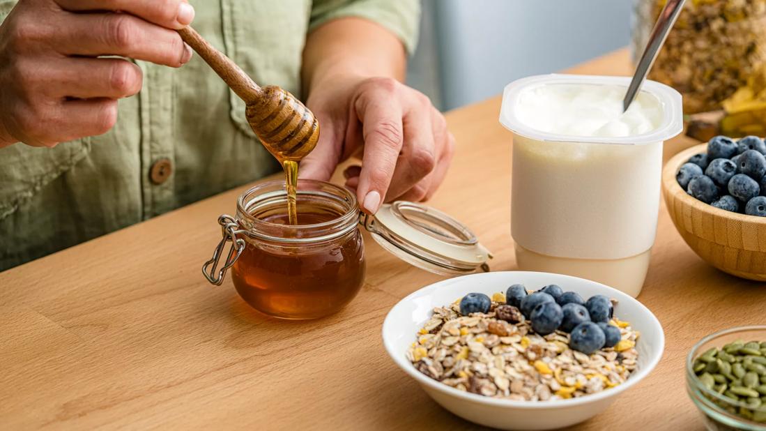 Person getting honey from a jar to put in bowl of oats, fruit and yogurt