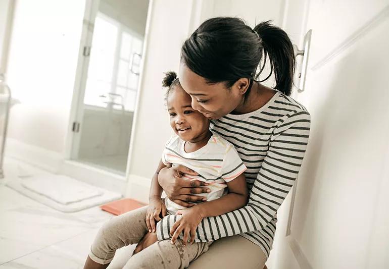 A mother hugging her toddler as both are sitting in a bathroom