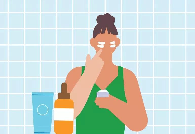 Person in bathroom applying cream to face with other products in foreground.