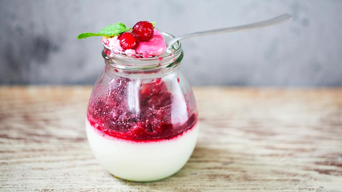 Red berry sauce over glass container of yogurt, with spoon balanced on top