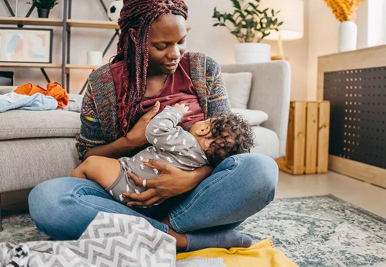 Parent breastfeeding their baby while sitting on the floor in their living room.