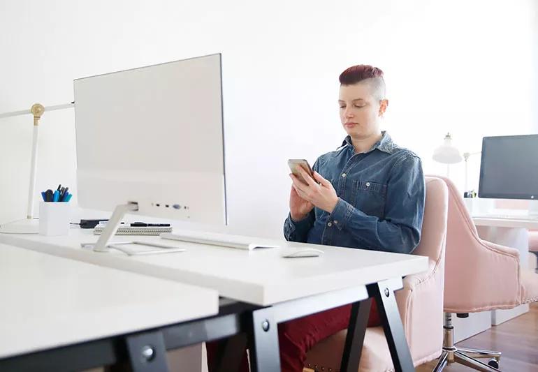 A person sitting at a desk and looking at their phone