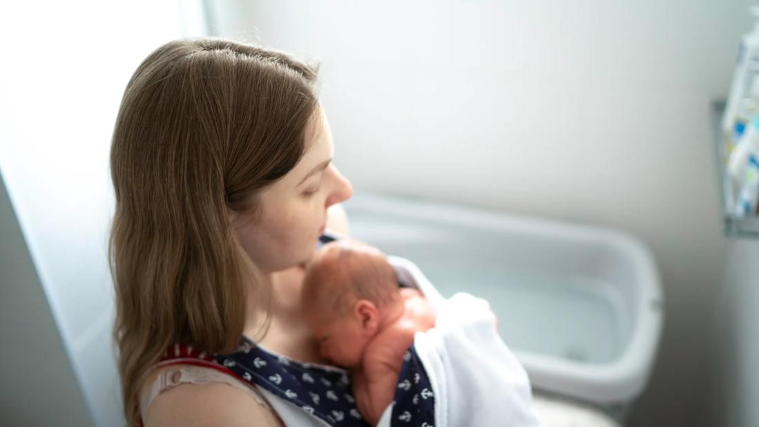 Caregiver holding newborn on chest, with bathtub filling in background