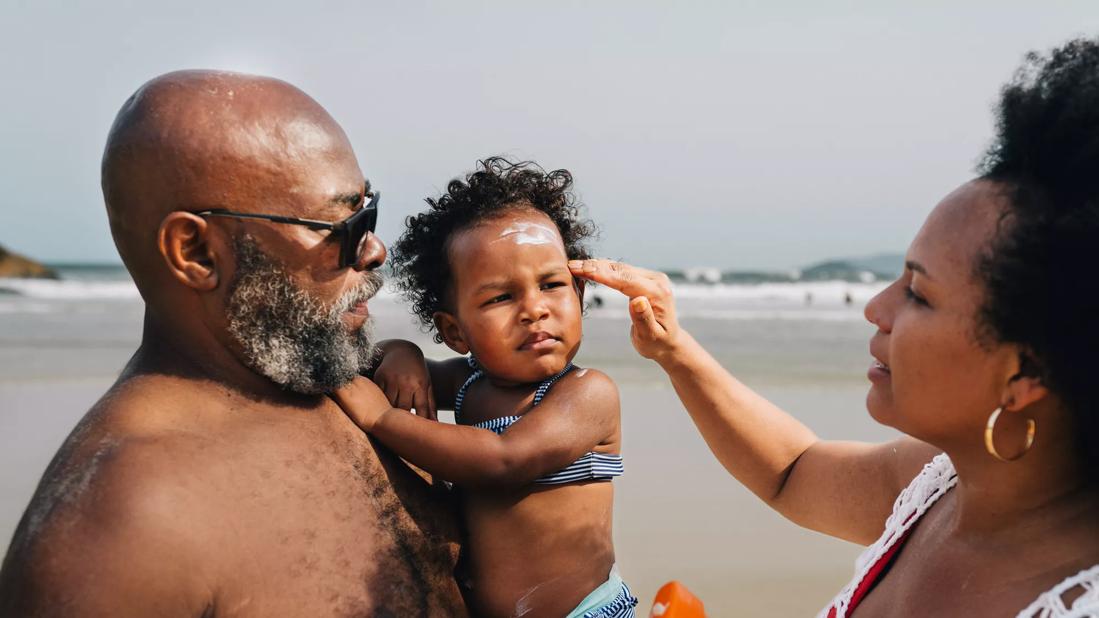 Parents applying sunscreen to their toddler at the beach