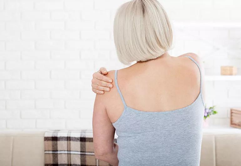 A person reaches back and grabs their shoulder because of discomfort.