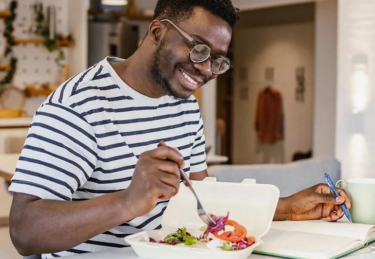 Man eating a healthy salad while sitting in the kitchen at home.