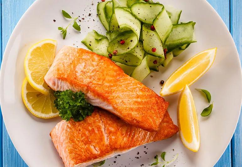 A plate of grilled salmon, a cucumber salad and lemon wedges and slices