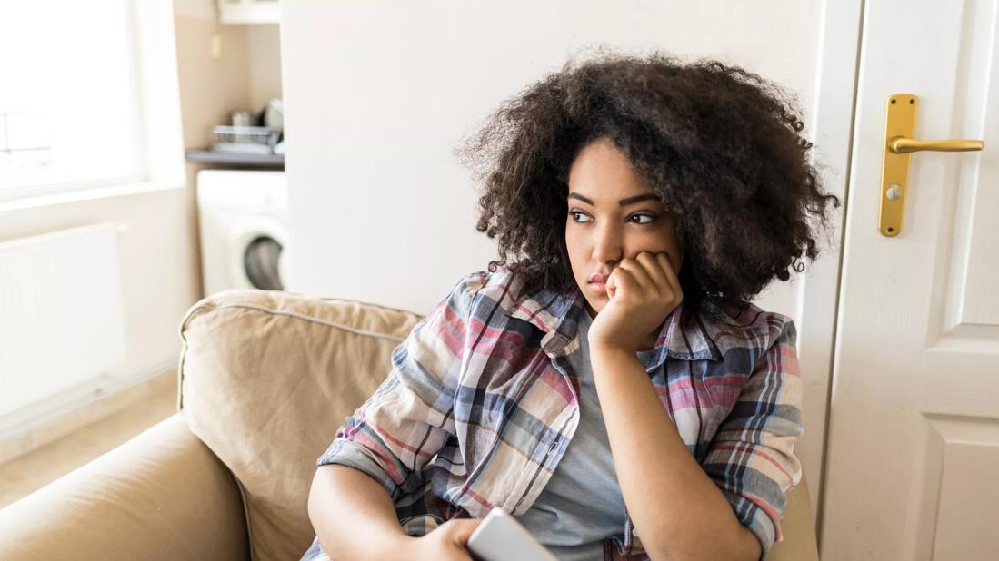 Female sitting in chair at home staring into the distance, phone in hand